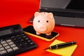 Moneybox near laptop and smartphone with sticky note. Finance and budget concept. Piggy bank in pink color with gadgets