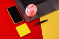 Moneybox near laptop and smartphone with sticky note, place for text. Finance and budget concept. Piggy bank in pink