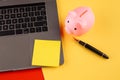 Moneybox near laptop and yellow sticky note, place for text. Finance and budget concept. Piggy bank in pink color with