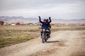 Mongolia Ulgii 2019-05-04 Mongolian men ride motorbike at steppe field on village background ang send greetings. Concept authentic