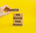 Progress symbol. Wooden blocks with words Monitor and Measure your Progress. Beautiful yellow background. Businessman hand.