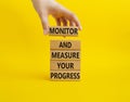 Progress symbol. Wooden blocks with words Monitor and Measure your Progress. Beautiful yellow background. Businessman hand.