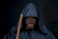 A monk in a black hood with a staff on a dark background, a gloomy expression, a medium plan, witchcraft and curses. Royalty Free Stock Photo