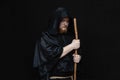 A monk in a black hood with a staff on a dark background, a gloomy expression, a medium plan, witchcraft and curses. Royalty Free Stock Photo