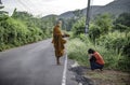 A monk comes out to offer alms by walking along a road surrounded by mountains in Suan Phueng District