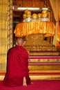 Monk praying in front of shrine with sacred Buddha figures