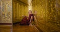 Monk in red robes prays in gold temple