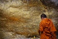 Monk respect praying and gild cover with gold leaf at Lord Buddha image appearing on a cave wall