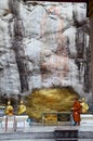 Monk respect praying and gild cover with gold leaf at Lord Buddha image appearing on a cave wall Royalty Free Stock Photo