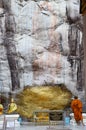 Monk respect praying and gild cover with gold leaf at Lord Buddha image appearing on a cave wall Royalty Free Stock Photo