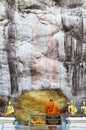 Monk respect praying and gild cover with gold leaf at Lord Buddha image appearing on a cave wall Royalty Free Stock Photo