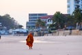 A monk walking on sand beach before residences in early morning