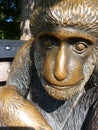 A small sculpture of a monkey sitting on a sunny park bench