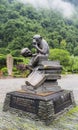 A monkey sitting on books holding a human crane statue at the garden of the Yellow Dragon Cave, Zhangjiajie, Hunan Province, China