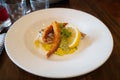 Monkfish with monkfish scampi on a bed of saffron and pesto risotto and a lemon garnish in a white dish on a wooden table Royalty Free Stock Photo