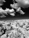 Monochome surreal image of a harsh rocky landscape in bright light with dark contrasting sky and white clouds