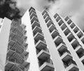 Monochrome angled detail view of an old 1960s white concrete apartment building with steps and balconies against sky and clouds