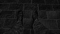 Monochrome black and white image. Feet in boots against the background of street tiles or the road. Two legs of a seated