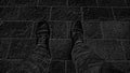 Monochrome black and white image. Feet in boots against the background of street tiles or the road. Two legs of a seated