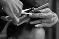 Monochrome closeup hands of barber holds scissors and comb while cutting the hair of little boy