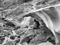 Monochrome image adult woman with backpack sitting on a rock under a block of ice