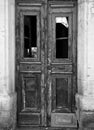 Monochrome image of a broken old double door in an abandoned derelict house with broken windows and faded peeling paint