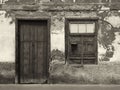 Monochrome image of the front of an old abandoned house with shuttered windows and locked wooden door with flaking peeling paint
