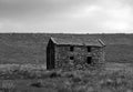 Monochrome image of a an old abandoned stone farmhouse in green pasture on high moorland with cloudy overcast sky