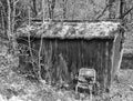 Monochrome image of an old abandoned wooden shack in woodland with broken chair outside and moss covered roof Royalty Free Stock Photo