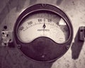 Monochrome image of an old round metal industrial ammeter with an analogue dial and scale