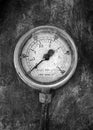 Monochrome image of an round industrial pressure gauge with numbers round the dial mounted on a metal surface Royalty Free Stock Photo