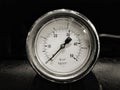 monochrome image of a round shiny pressurevintage gauge with numbers marked in psi and metric on the meter dial on industrial