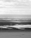 Monochrome image of a single figure walking alone across a dark beach under a cloudy sky