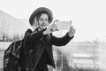 Monochrome image.Tourist woman in hat with backpack stands at airport, takes photos, shoots video on smartphone`s camera Royalty Free Stock Photo