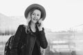 Monochrome image. Young tourist woman in hat and with backpack is standing at airport and talking on cell phone. Royalty Free Stock Photo