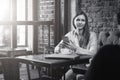 Monochrome image.Young woman sits at table in cafe and use smartphone.On table is cup of coffee and closed notebook