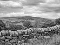 Monochrome landscape image of a dry stone wall in front of a tree lined valley with yorkshire dales scenery and village houses in Royalty Free Stock Photo