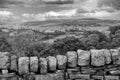 Monochrome landscape image of a dry stone wall in front of a tree lined valley with yorkshire dales scenery and village houses in Royalty Free Stock Photo