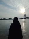 Monochrome muslim woman silhouette enjoying the sunset by the beach under the EMAS bridge. Royalty Free Stock Photo