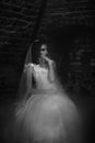 Monochrome mysterious bride sitting pensively in wine cellar by a window