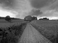 Monochrome perspective view of a long narrow country lane bordered by fences and stone walls with dark cloudy sky