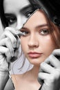 Monochrome portrait of female with mirror shard in hand posing on gray background. Color face reflection in mirror splinter