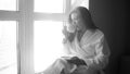 Black and white portrait of young woman sitting at window and drinking tea Royalty Free Stock Photo