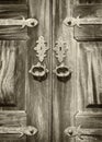 Monochrome sepia close up of ancient varnished wooden double doors with ornate metal decorative keyholes and handles