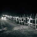 Monochrome shot of a car with headlights on driving on a rural road at night, by the wooden fence