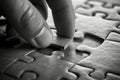 Monochrome shot of a finger pressing a single puzzle piece onto a textured board Royalty Free Stock Photo