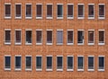 Monotonous facade of red bricks of a high-rise office building with long rectangular windows without curtains in the city center Royalty Free Stock Photo