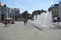 The elegant town square in the handsome Belgian city of Mons. People walk by a water feature.