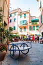 Blue cart with two wheels standing on a cozy street full of vibrant buildings, walking people, shops and bars in Monterosso Al