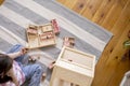 Montessori material. Child girl in pink T-shirt arranges wooden furniture in a doll house. Flat lay